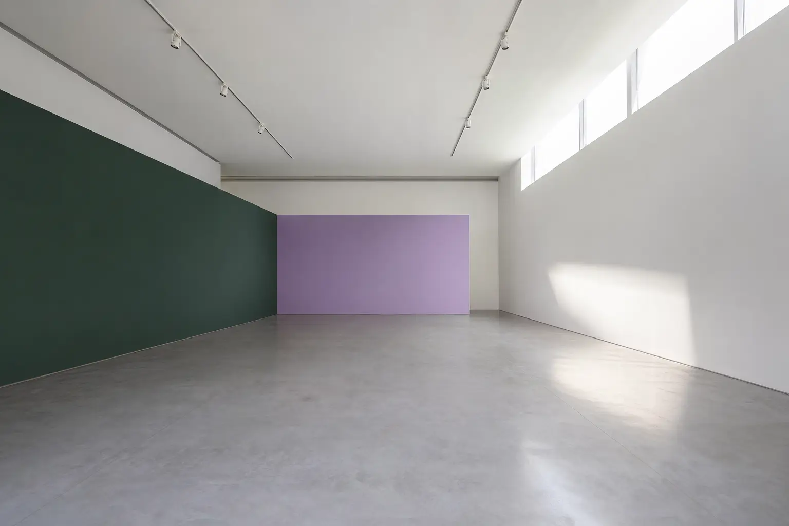 An empty gallery room with a polished concrete floor and one high window