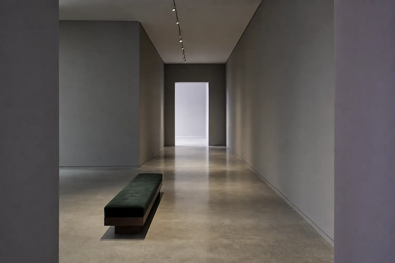 A long gallery corridor with a bench and a doorway at the end