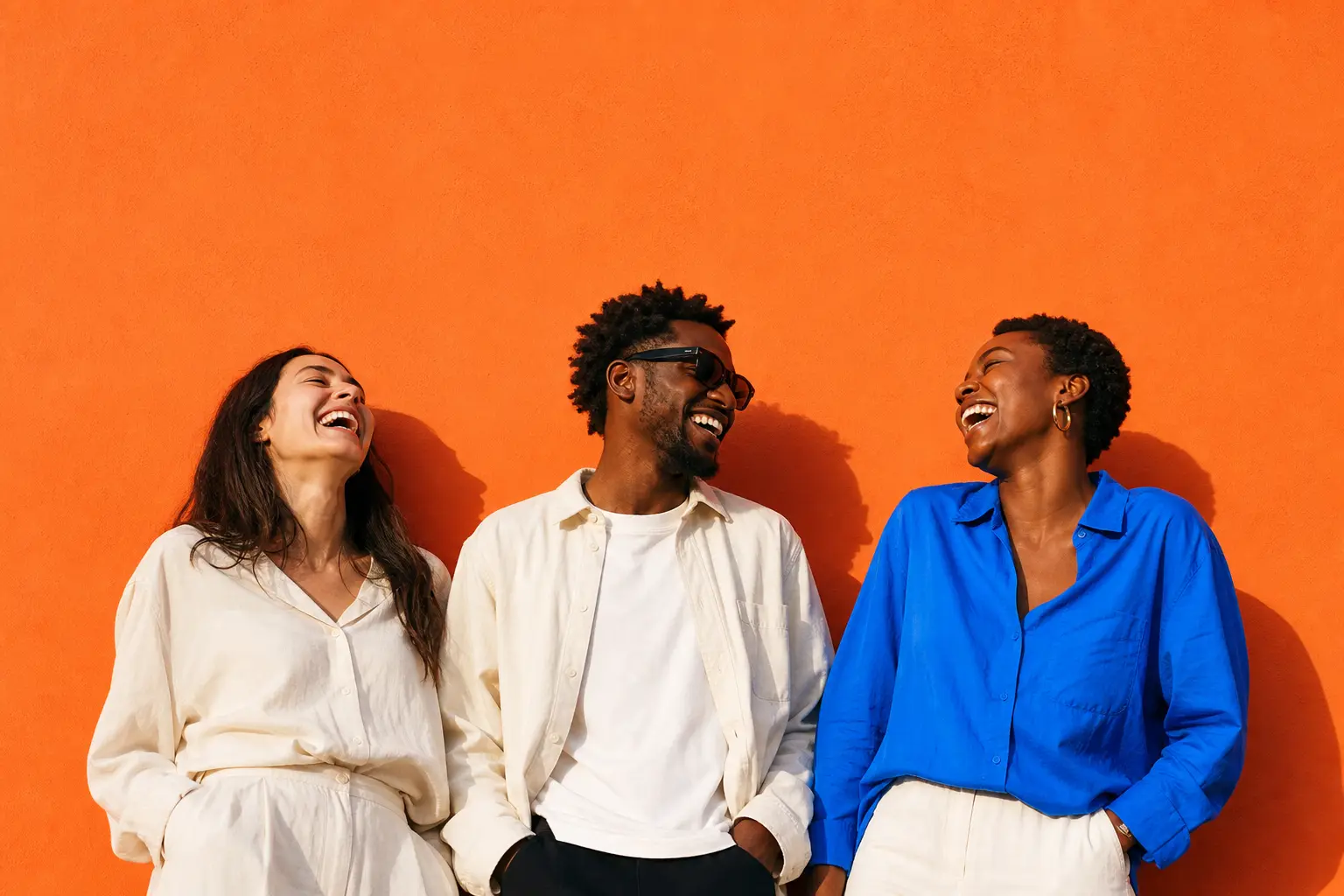 Friends laughing together against a bright orange wall