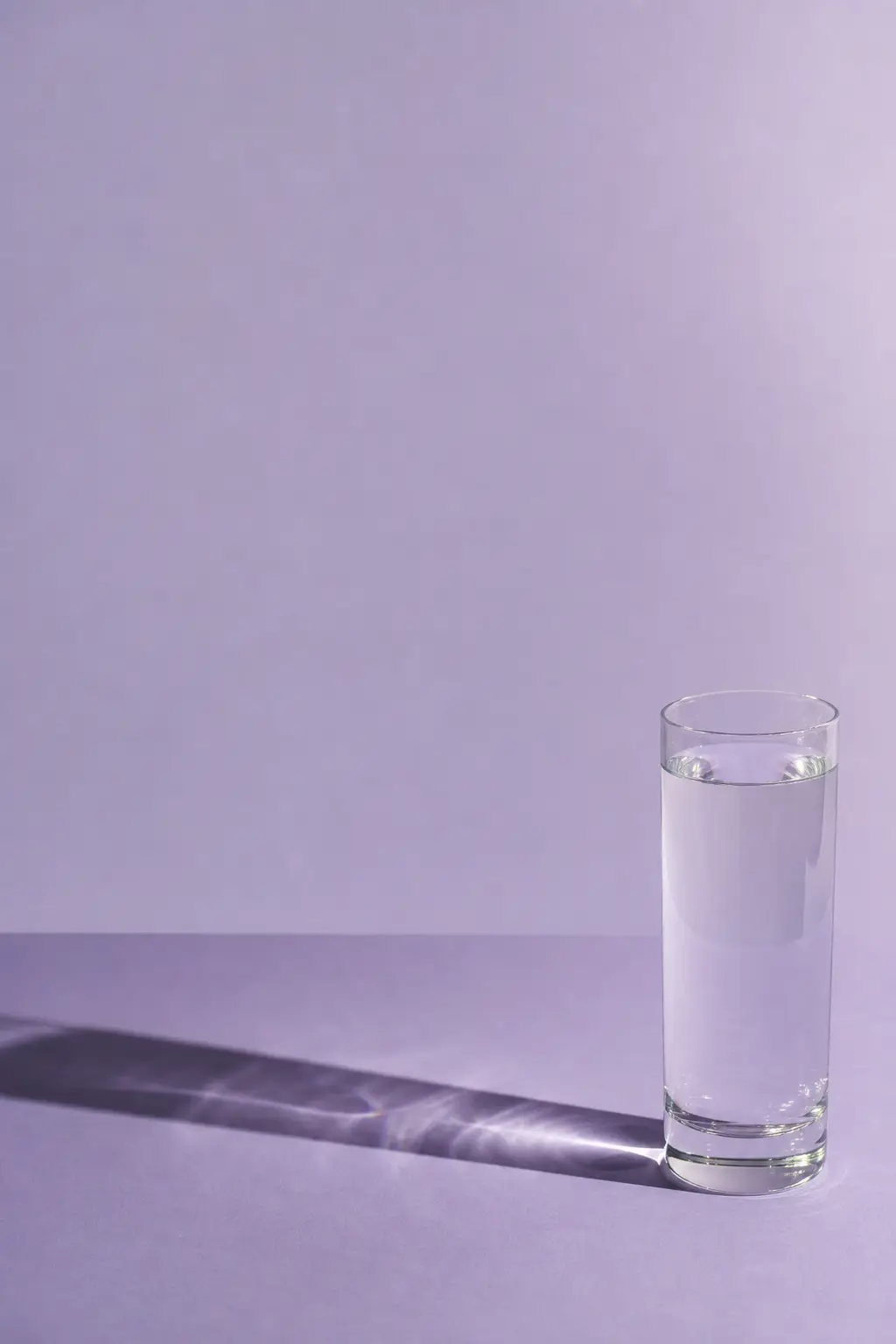 A tall glass of water on a pale surface with a hard shadow